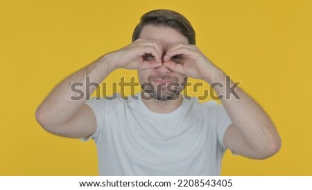 Happy Man Searching with Handmade Binocular on Yellow Background