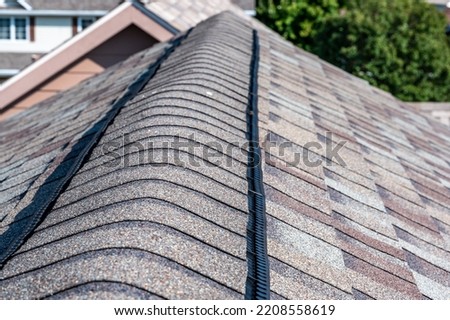 Ridge cap vent installed on a shingle roof for passive attic ventilation on a residential house.  Royalty-Free Stock Photo #2208558619