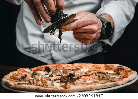 Pizza with black truffle and porcini mushroom. Special edition for an Italian Restaurant. A chef slices truffles on pizza.
