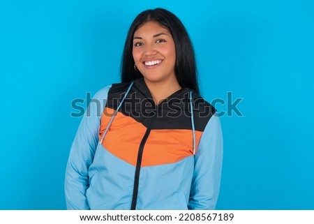 Young latin woman wearing sport clothes over blue background with broad smile, shows white teeth, feeling confident rejoices having day off.