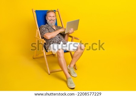 Full size photo of cheerful aged man sit lounger use wireless netbook isolated on yellow color background