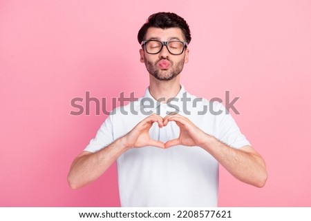 Portrait photo of young attractive handsome positive guy wear glasses white polo t-shirt showing love symbol pouted lips kiss air isolated on pink color background