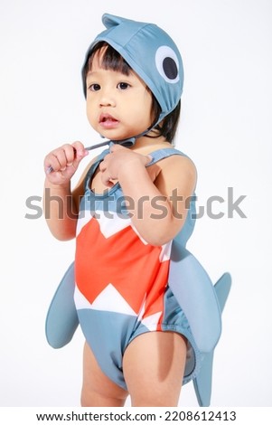 Studio shot of little beautiful kindergarten Asian baby girl daughter model in cute gray shark costume swimsuit outfit standing on white background
