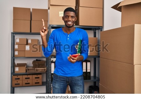 African american man working at small business ecommerce using smartphone smiling with an idea or question pointing finger with happy face, number one 