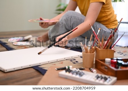Young woman holds color palette and point over blank canvas, ready for start painting. Art, hobby and leisure activity concept
