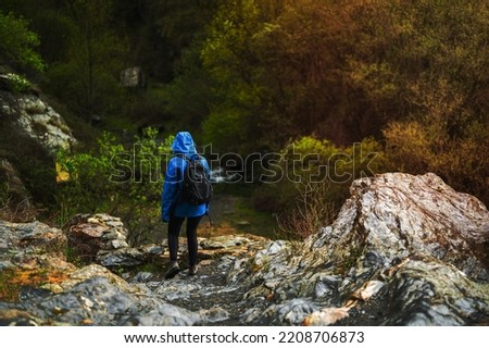 girl with blue jacket walking on the mountain while raining with vegetation in the background.