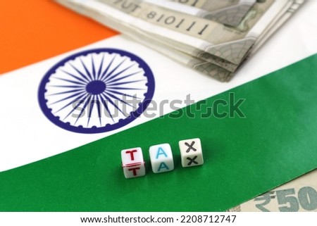 The word Tax on the background of the Indian flag and rupees. Taxation in India. Selective focus. Shallow depth of field.