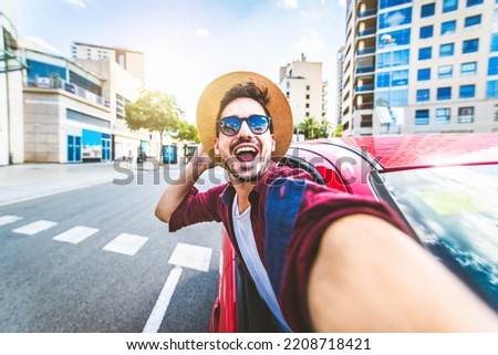 Young handsome man taking selfie picture in the car - Happy tourist driving a rental car on city street - Transportation, travel and vacations concept