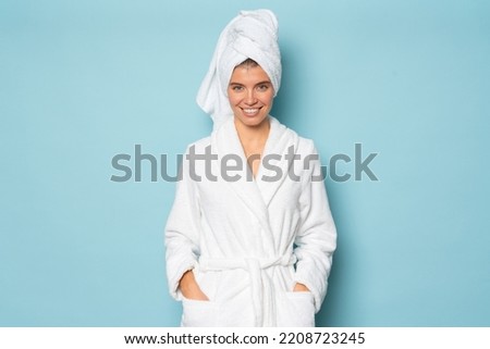 Smiling woman with clean body wearing white bathrobe and towel on head standing on blue studio background with hands in pocket at spa day on vacation or weekend. Hygiene, purity concept Royalty-Free Stock Photo #2208723245