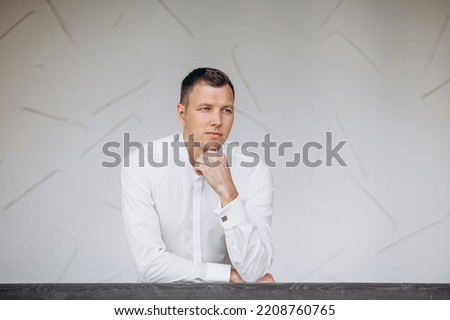 Handsome young adult man in a white shirt, portrait against a white wall