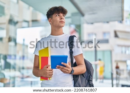 Young hispanic teenager student using touchpad holding books at university Royalty-Free Stock Photo #2208761807