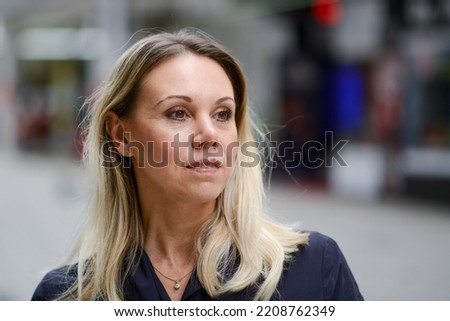 Side view of an attractive middle aged blonde woman wearing a blue jacket with a slight smile while shopping against an urban backdrop on a shopping street Royalty-Free Stock Photo #2208762349