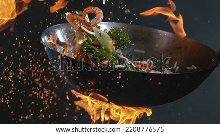 Freeze Motion of Wok Pan with Flying Ingredients in the Air and Fire Flames. Royalty-Free Stock Photo #2208776575