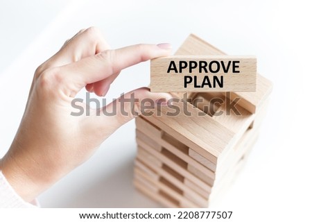 APPROVE PLAN inscription on a wooden bar in a person's hand on a light background