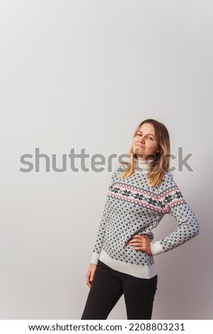 Russian girl in a knitted pullover on a white wall. Slav girl in a Turkish knitted New Year's sweater on a light wall. Christmas sweater with stars on a woman for a photo shoot