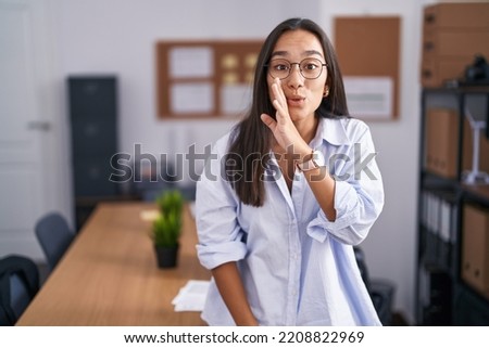 Young hispanic woman at the office hand on mouth telling secret rumor, whispering malicious talk conversation  Royalty-Free Stock Photo #2208822969