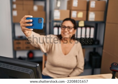 Middle age hispanic woman ecommerce business worker making selfie by the smartphone at office