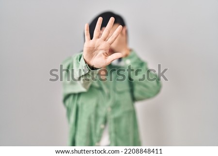 Young asian woman standing over white background covering eyes with hands and doing stop gesture with sad and fear expression. embarrassed and negative concept. 