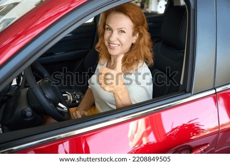 Satisfied woman sits behind the wheel of car shows ok