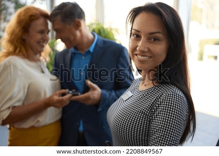 Smiling car dealership employee against the background of satisfied customers