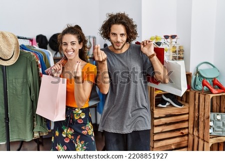 Young hispanic couple holding shopping bags at retail shop doing italian gesture with hand and fingers confident expression 
