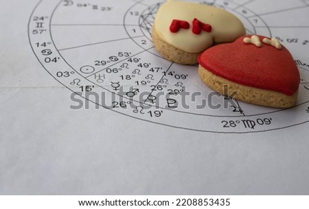 Close up of printed astrology chart with Venus, Pluto and Mars planets; heart shaped cookies in the background, astrology love concept