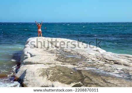 View from back of slender girl in bikini on edge of cliff overlooking the Mediterranean Sea