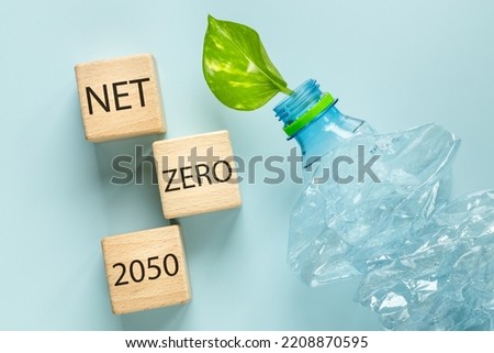 A crushed plastic bottle with a young green leaf growing out of it, wooden blocks with the words Net Zero 2050, Environmental concept, Reduction of greenhouse gas emissions and plastic recycling Royalty-Free Stock Photo #2208870595