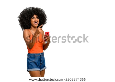 positively surprised young woman points to a white space, holds a smart phone in one hand, black power style hair