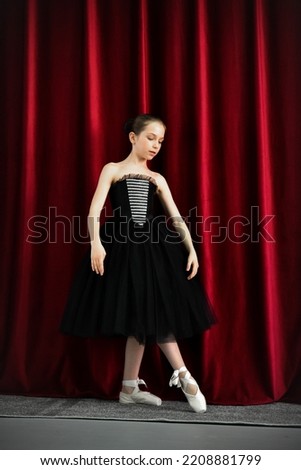 A cute ballerina girl in a black dress on a red background. Art. Dance. Beauty.