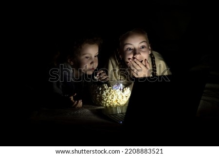 Two sister girls watch cartoons on the device and have a fun together. They're at home. Childhood. Leisure.