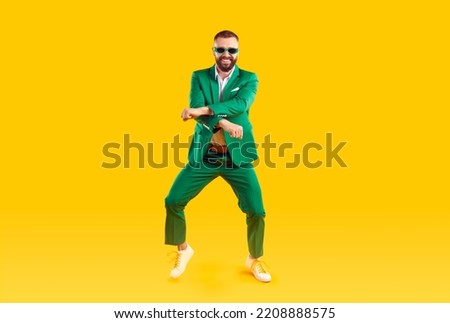Cheerful and stylish man is having fun dancing in Gangnam style at St. Patrick's Day party. Young man in trendy youth green suit and sunglasses is dancing and laughing on orange background. Banner. Royalty-Free Stock Photo #2208888575