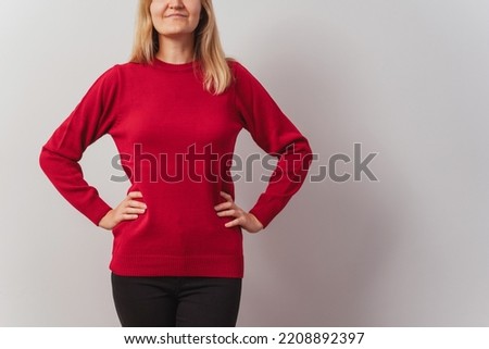 Russian girl in a knitted sweater on a white wall. Slav girl in a knitted New Year's pullover on a light wall. Christmas red sweater on a woman for a New Year's photo shoot