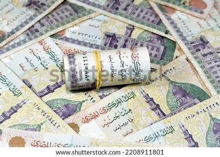 Egyptian money roll with rubber band of 200 LE EGP two hundred pounds on a pile of Egyptian cash money banknotes with Qani-Bay mosque and seated scribe, selective focus of Egypt currency rolled up Royalty-Free Stock Photo #2208911801