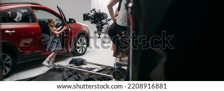 Professional actress girl works in the frame on the set. Shooting with a car on a large white cyclorama. Little girl 8 years old on the set of a movie, commercial or TV series. Filming indoors, studio Royalty-Free Stock Photo #2208916881