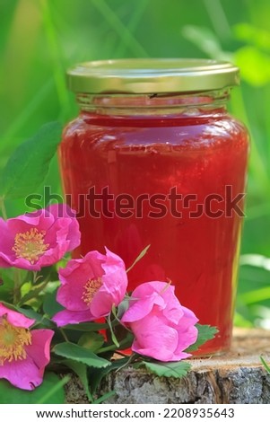 Wild rose jam in the glass jar and flowers on the stump in the forest.