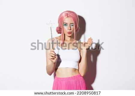 Portrait of attractive girl cosplay fairy for halloween, wearing pink wig and holding magic wand, standing over white background