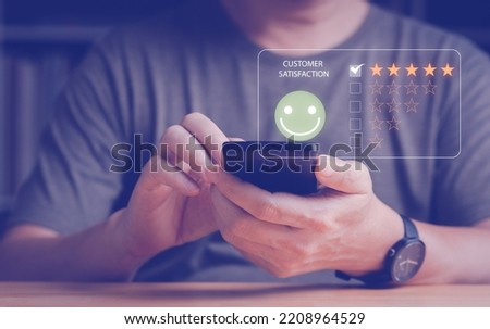 Man's hand give the customer satisfaction feedback with smart phone, review and rating with five gold stars and smiley face. Customer satisfaction feedback and survey concept. Royalty-Free Stock Photo #2208964529