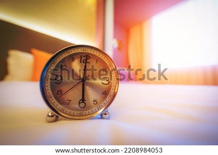 Alarm clock on the bed in morning time with sunlight.