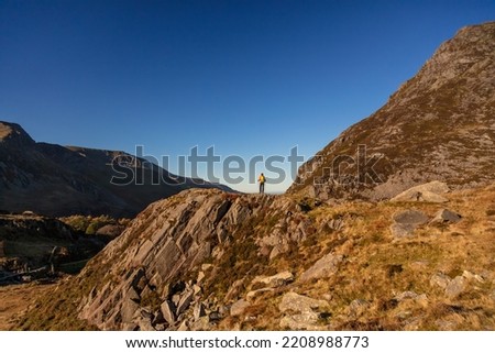 Freedom outdoors for adventurous female hiker exploring remote trails over rugged mountainous terrain of Snowdonia National Park Wales Royalty-Free Stock Photo #2208988773