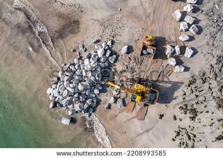 aerial view directly above Mechanical diggers on a construction site repairing coast defences and sea walls with rocks from a quarry after rising sea levels caused erosion and damage Royalty-Free Stock Photo #2208993585
