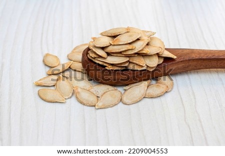 Dry Pumpkin Seeds in a Wooden Spoon Isolated on White Wooden Background