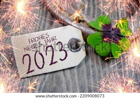 Wooden hang tag and slate with four leaf clover and sparklers with the german words for happy new year - frohes neues jahr 2023 on wooden weathered background	