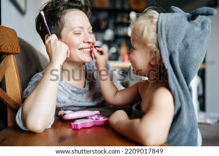 mother and child use cosmetics together. With a smile, the daughter paints her mother's lips at home. Growing up.