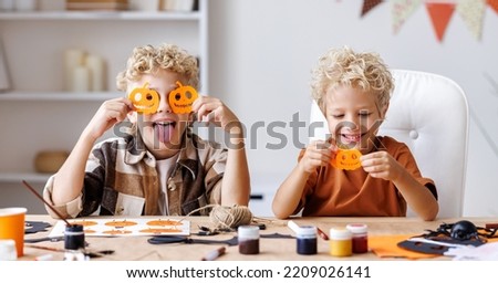 Portrait of cute kids  boys  making Halloween home decorations   while sitting at wooden table, children covers eyes with carved pumpkins and laughs 