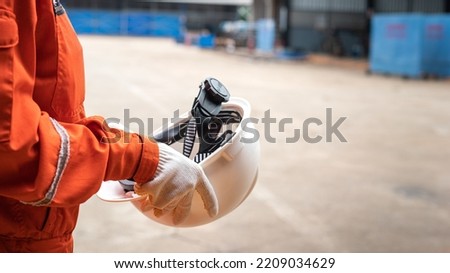 Action of a worker is preparing to wear a white safety hardhat with blurred background of factory workplace. Industrial safe work practice concept photo, selective focus.