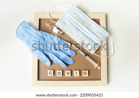 White isolated background, on the table lies a frame inside her syringe and ampoule, a protective mask and gloves, cubes with text.  Concept, theme of vaccination and covid 19 renovation. Flat lay.