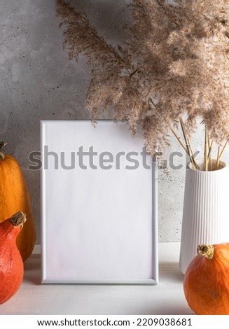 Empty white frame with space for text, pumpkins, dry grass on light neutral background. Mock up.