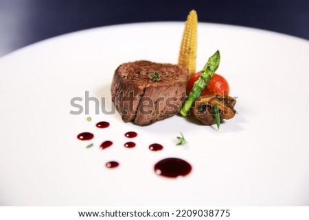 Tender grilled piece of meat with sauce on a white plate with isolated background. Fillet minion with corn, asparagus and tomato. Side view.