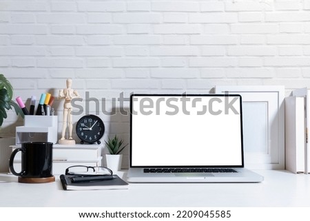Mock up laptop with blank screen, picture frame, books and stationery on white table.
